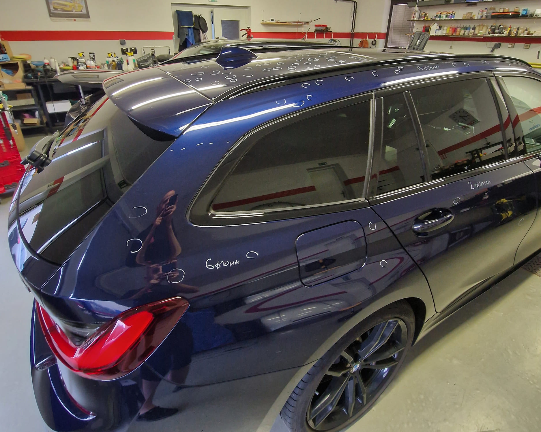 Plachta proti krupobití natažená na autě; technik pod LED panelem kontroluje promáčkliny