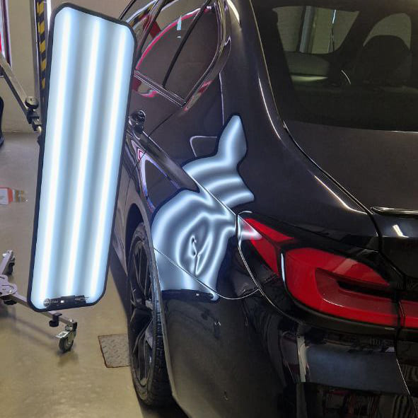 Осмотр кузова при возврате автомобиля из лизинга: мастер проверяет вмятины на двери под светом PDR-лампы